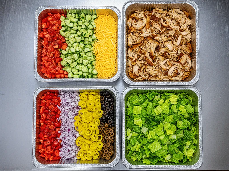 Catering pans of diced tomatoes, cucumbers, and shredded cheddar